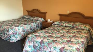 Two single beds with floral bedding, a wooden headboard, a nightstand with a phone, and a wall socket.