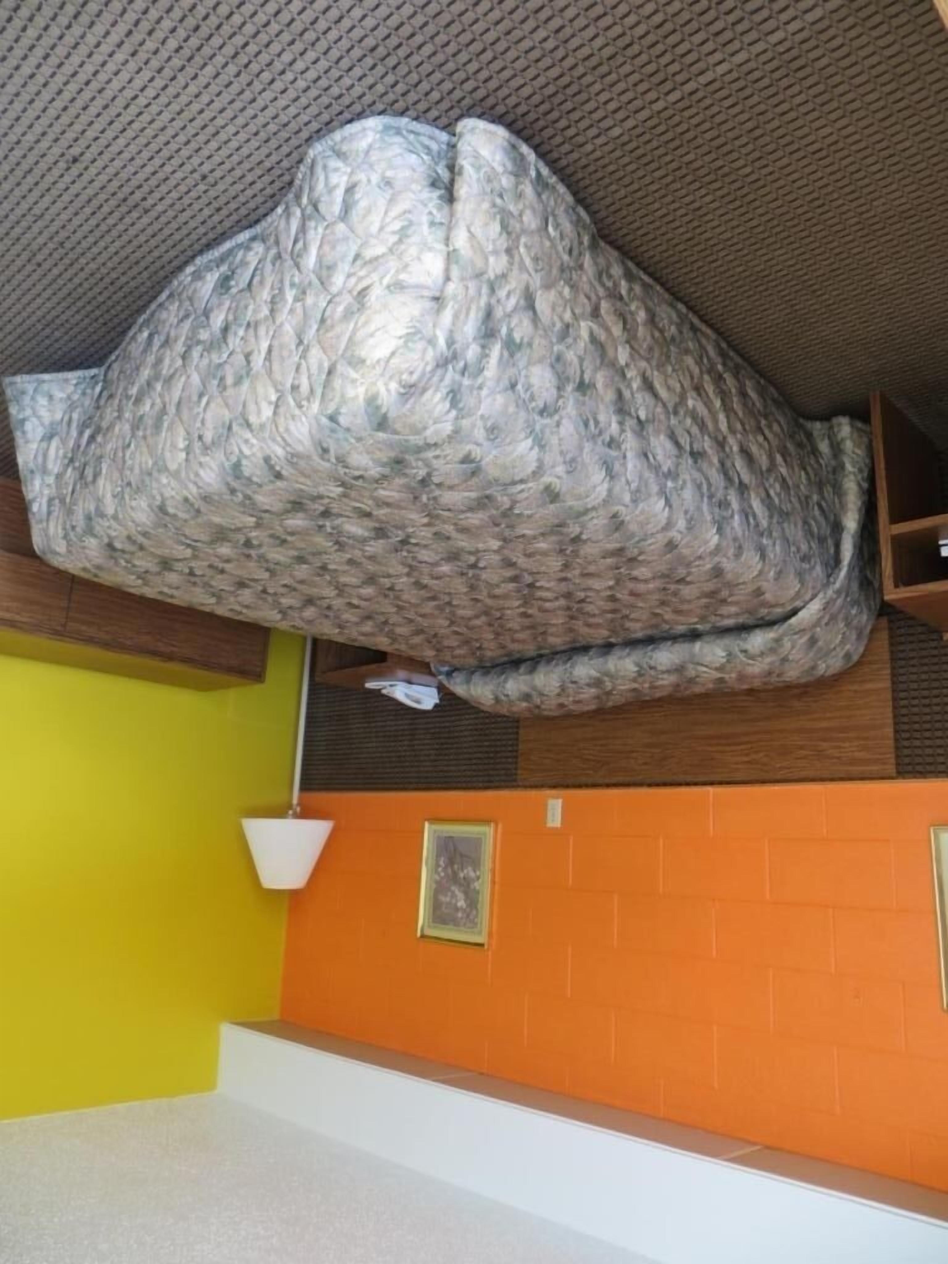A compact room with a bed, a small wooden shelf, and a bright orange wall.