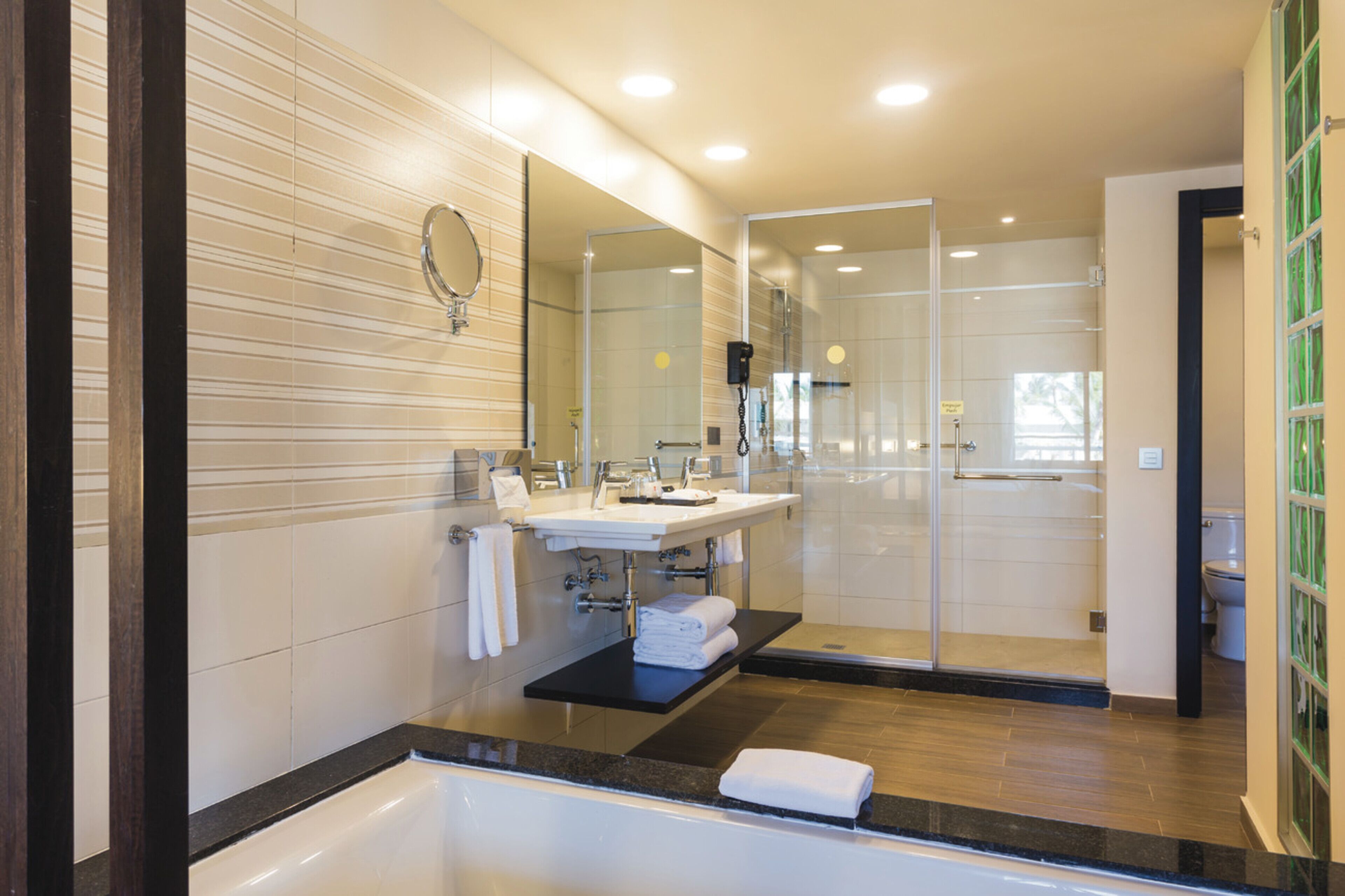 Un baño moderno con ducha de vidrio, un espejo grande y encimera negra.