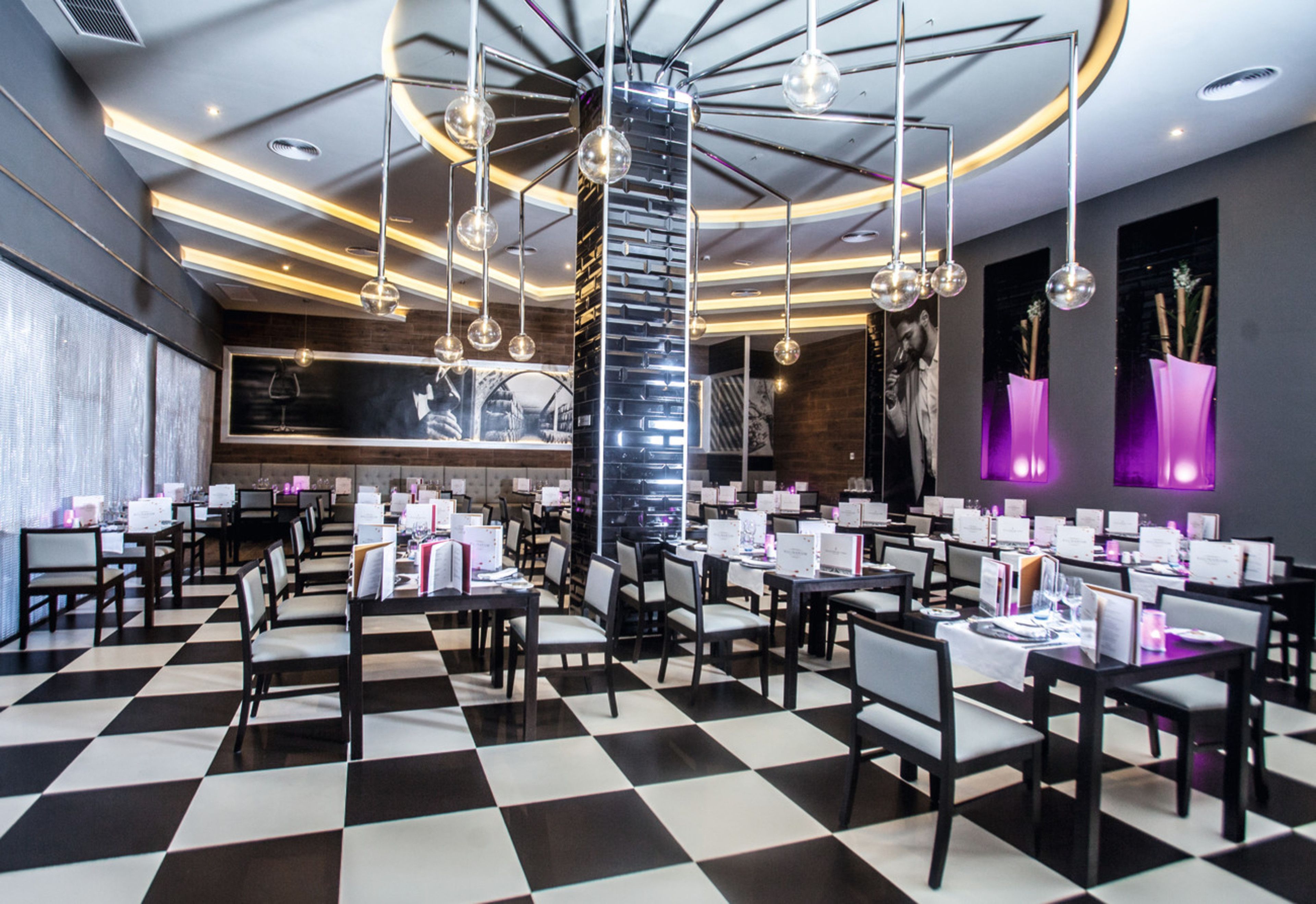 Um restaurante moderno com chão quadriculado, mesas redondas e luminárias esféricas pendentes.