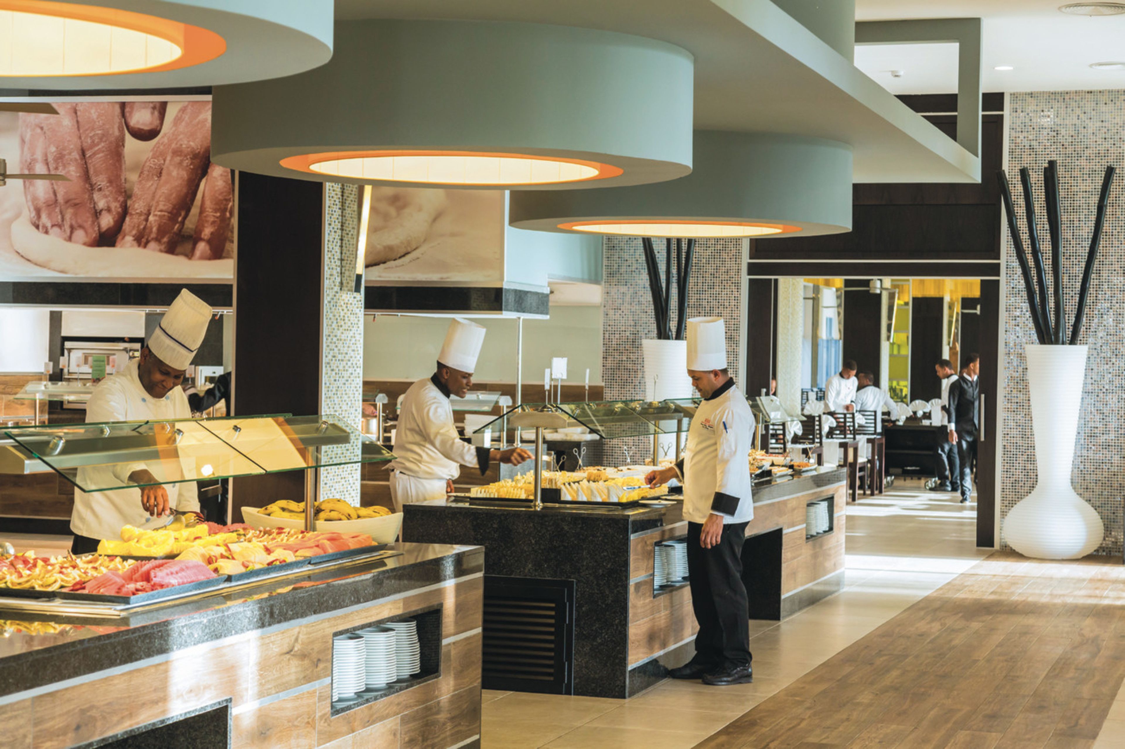 Zona de buffet con varias estaciones de servicio, un gran jarrón decorativo y un diseño interior moderno.