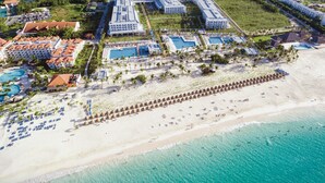 Vista aérea de un resort con varias piscinas, villas frente a la playa y una playa de arena.
