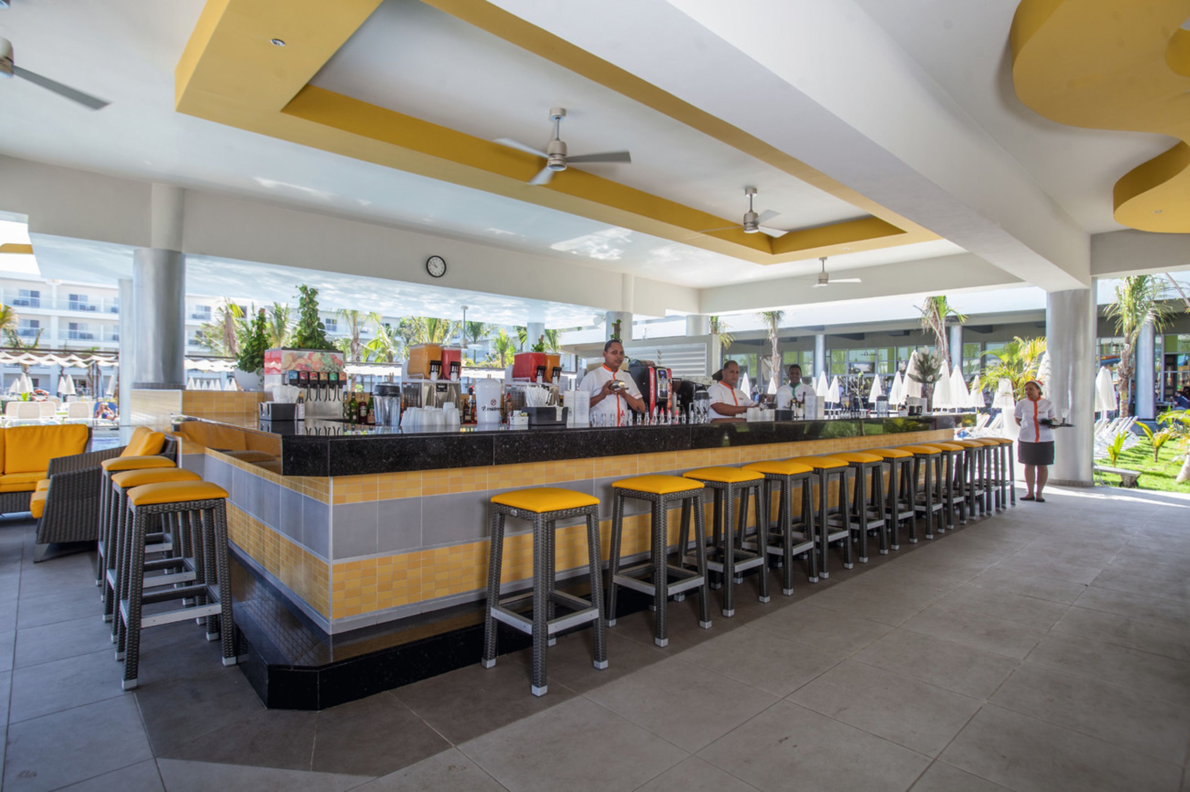 Un área de bar moderna con una barra larga, varios taburetes y un ventilador de techo.