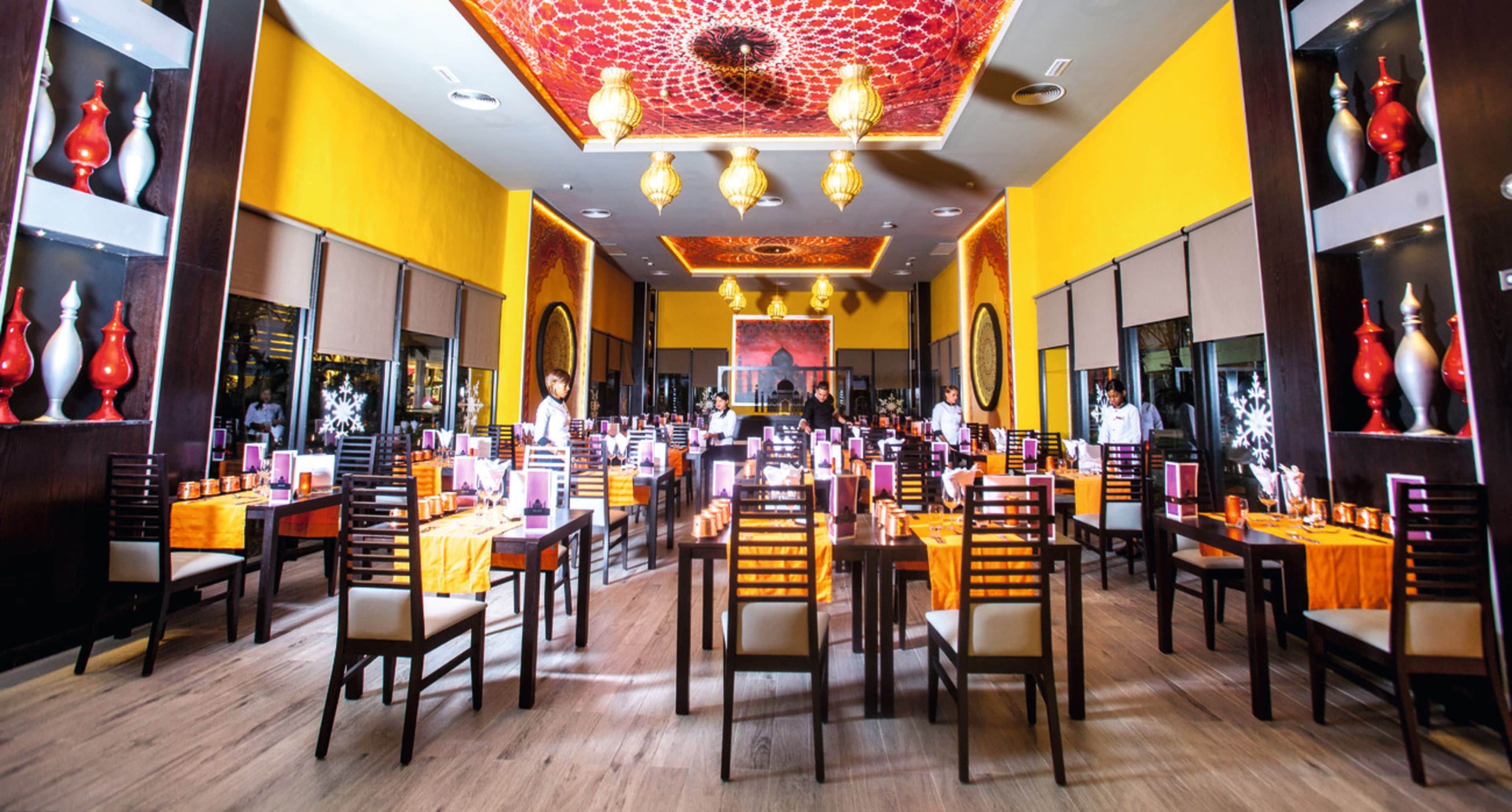 Un restaurant spacieux, doté de nombreuses tables et chaises, d’un plafond orné de motifs et de vases décoratifs accrochés aux murs.