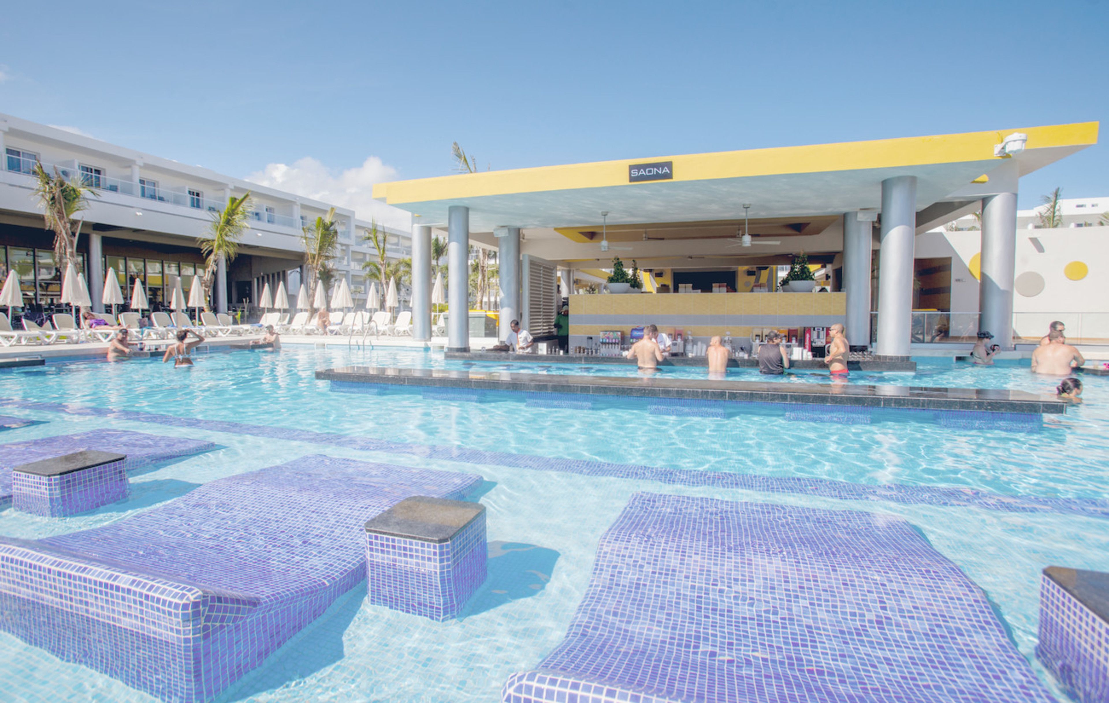 Una piscina con zonas de descanso con azulejos y una sección cubierta que dice 'SAONA'.