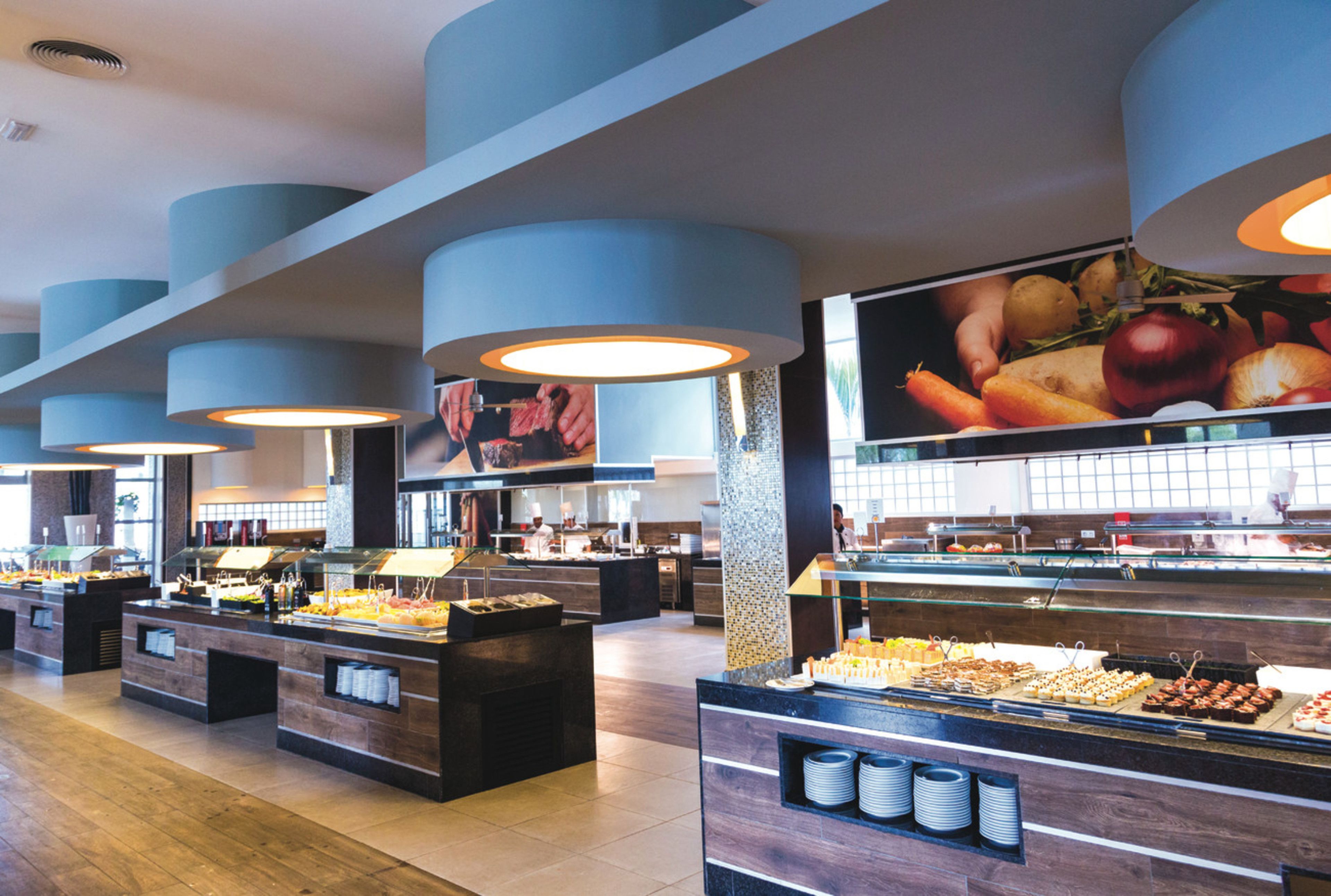 Een buffetgedeelte met diverse stations, een betegelde vloer en blauwe plafondlampen.