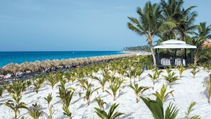 Una playa con sombrillas de paja, palmeras y un pabellón.