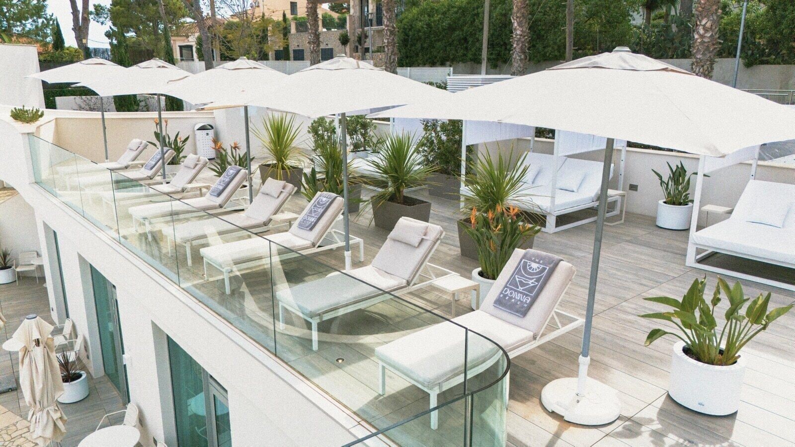A rooftop lounge area with glass balustrades, white lounge chairs, and umbrellas.