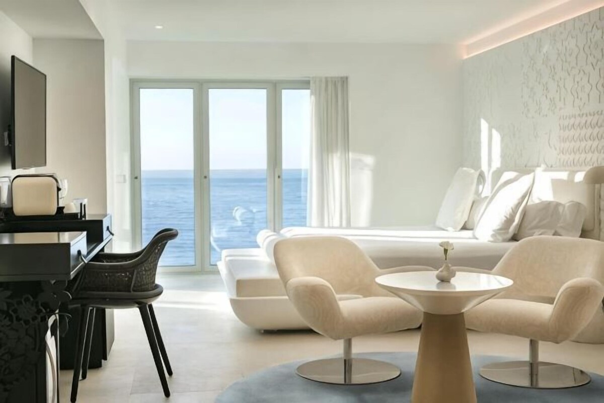 A modern hotel room with a large window, a sofa, a round table, and a TV.