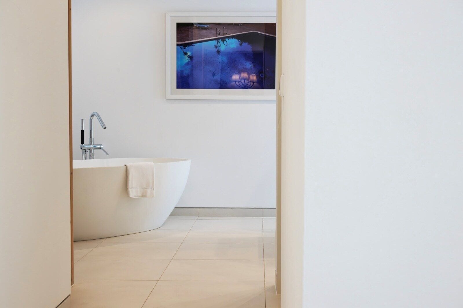 A modern bathroom with a freestanding bathtub, a wall-mounted sink, and a framed artwork above the bathtub.