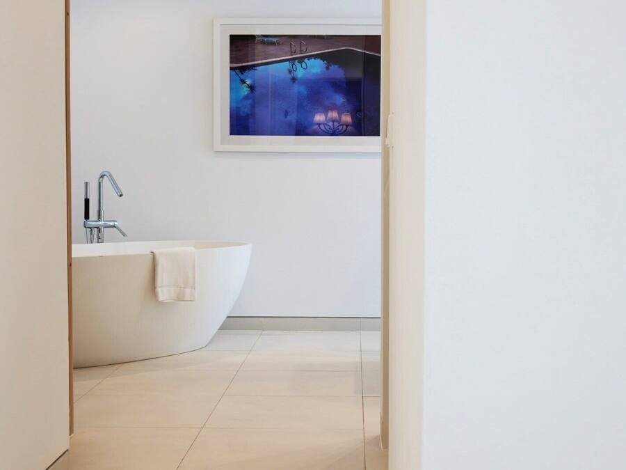 A modern bathroom with a freestanding bathtub, a wall-mounted sink, and a framed artwork above the bathtub.