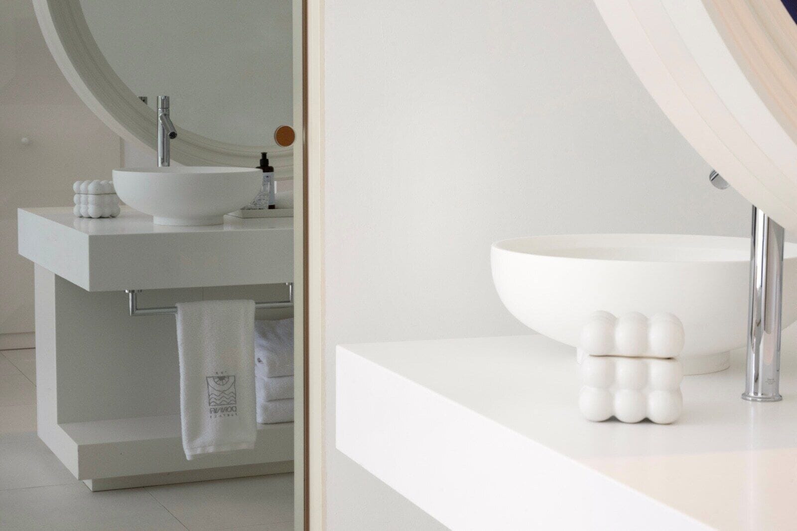 A modern bathroom with a white sink, a large mirror, and a towel rack.