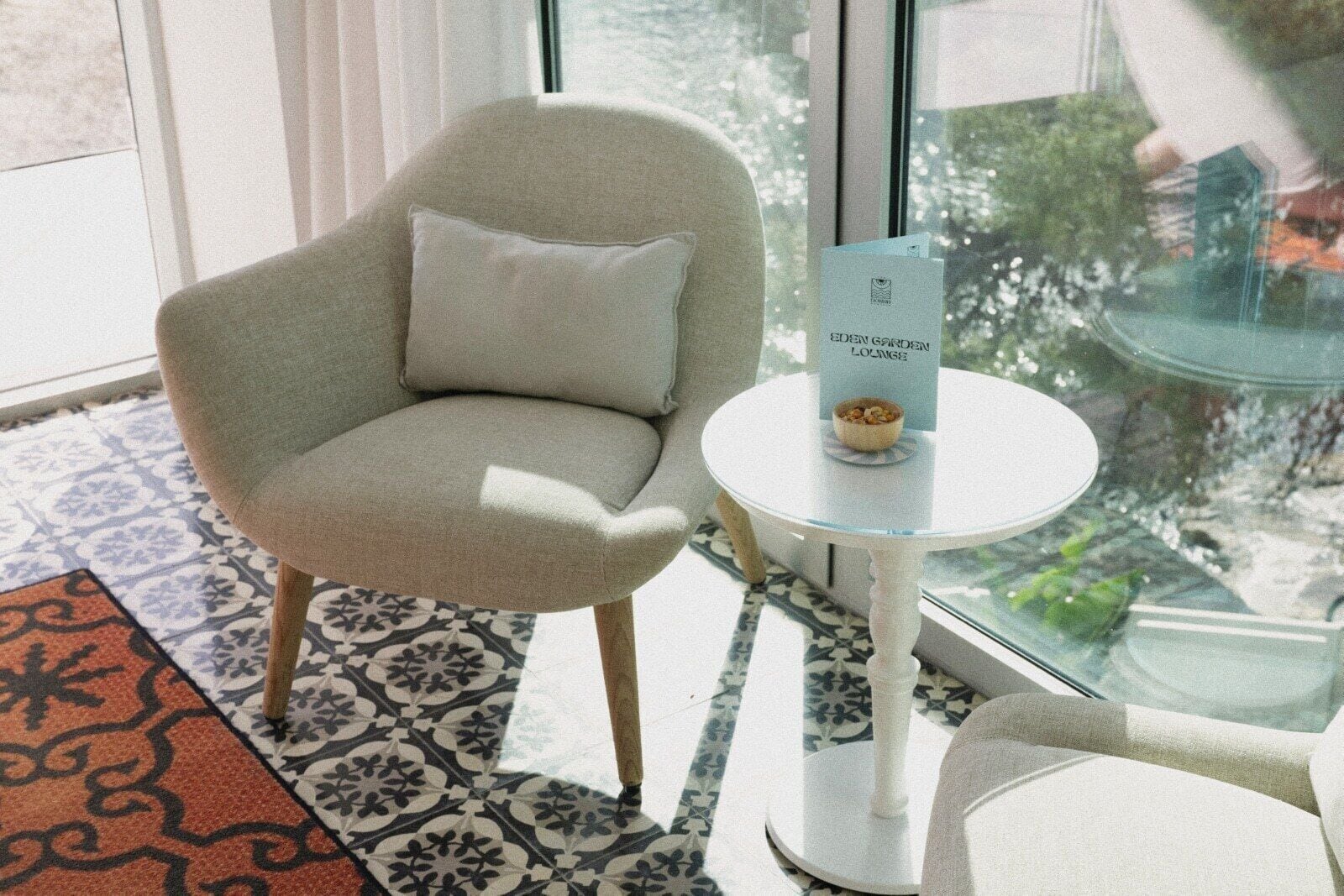 Un área de estar moderna con un sillón gris, una mesita redonda con un menú, y un suelo con diseño.