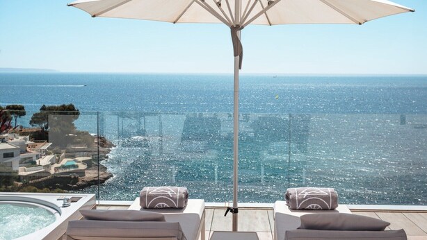 A balcony with a white umbrella, lounge chairs, and a view of the sea. - The Donna Portals (Calvia)