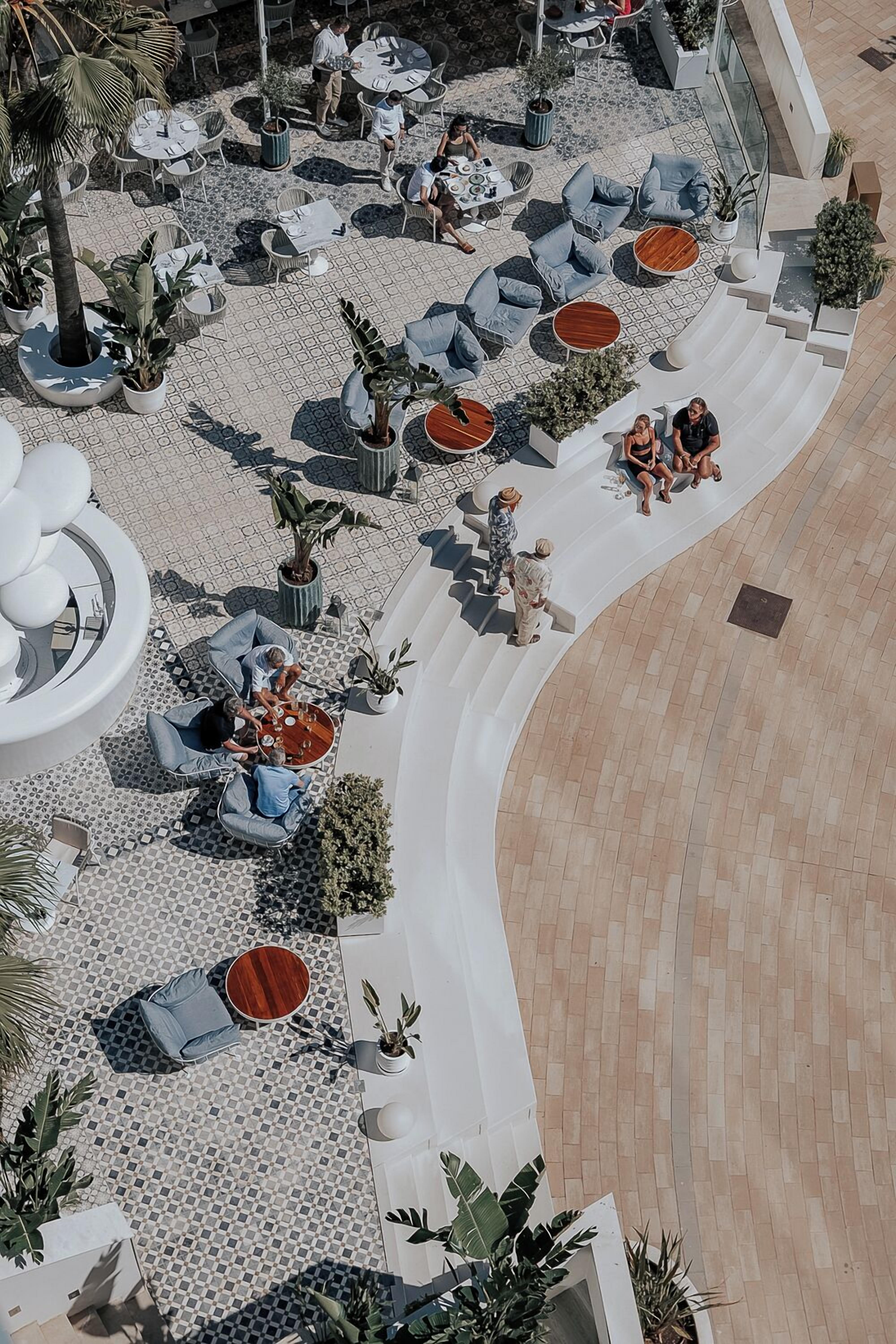 An outdoor patio area with seating arrangements, potted plants, and a curved pathway.