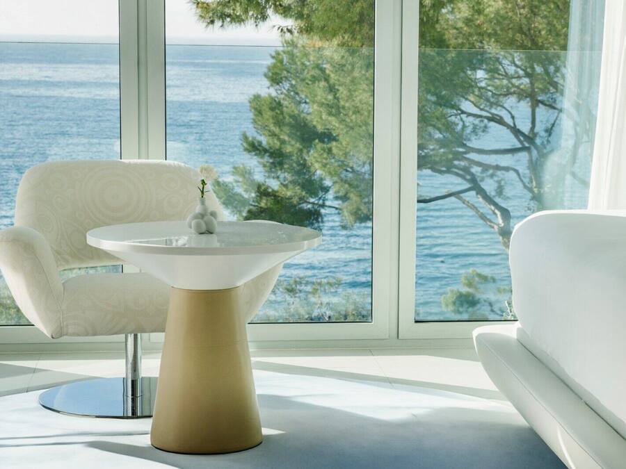 Un interior moderno con una silla y un sofá blancos frente a un ventanal con vista al mar.