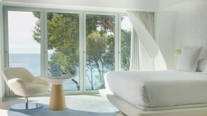 A modern bedroom with a large bed, a white chair, and a table with a book. - The Donna Portals (Calvia)