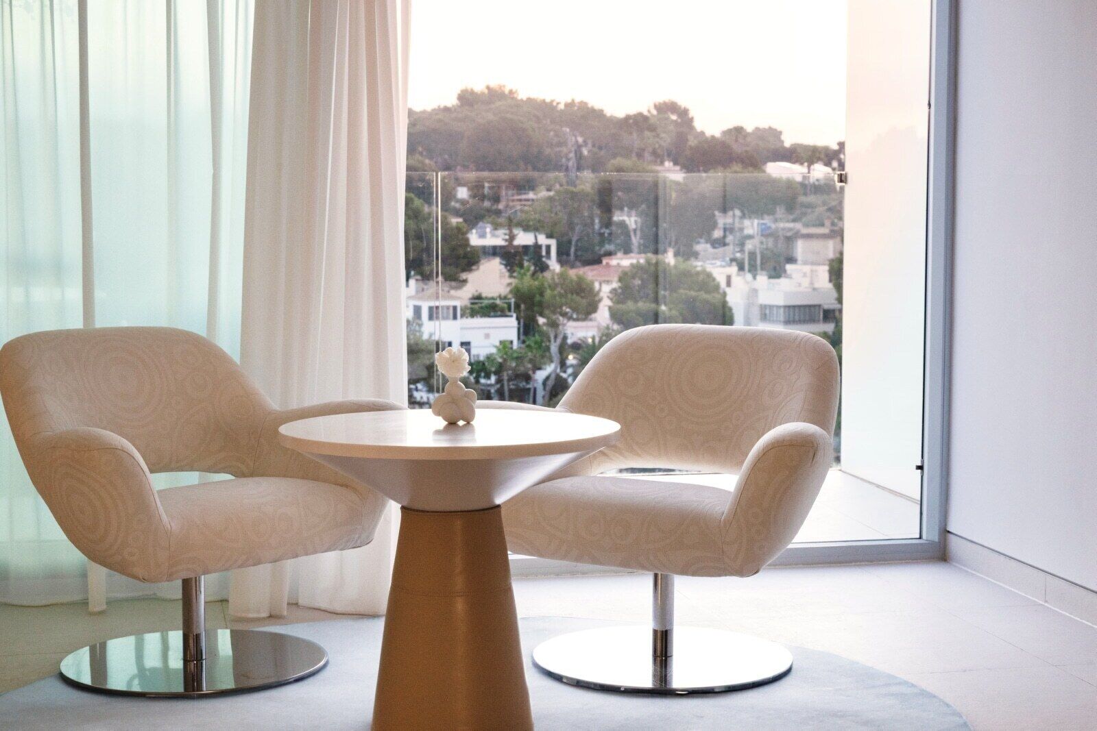 Une pièce moderne avec deux fauteuils et une table ronde, de grandes fenêtres offrant une vue sur le paysage urbain.