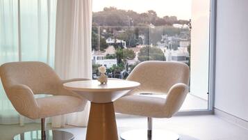 Une pièce moderne avec deux fauteuils et une table ronde, de grandes fenêtres offrant une vue sur le paysage urbain.