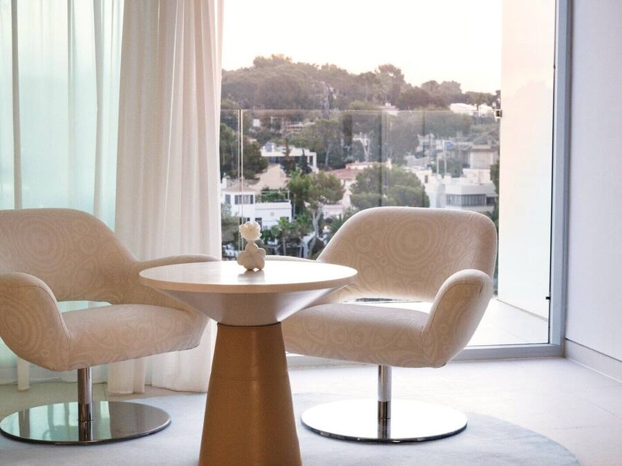 Une pièce moderne avec deux fauteuils et une table ronde, de grandes fenêtres offrant une vue sur le paysage urbain.