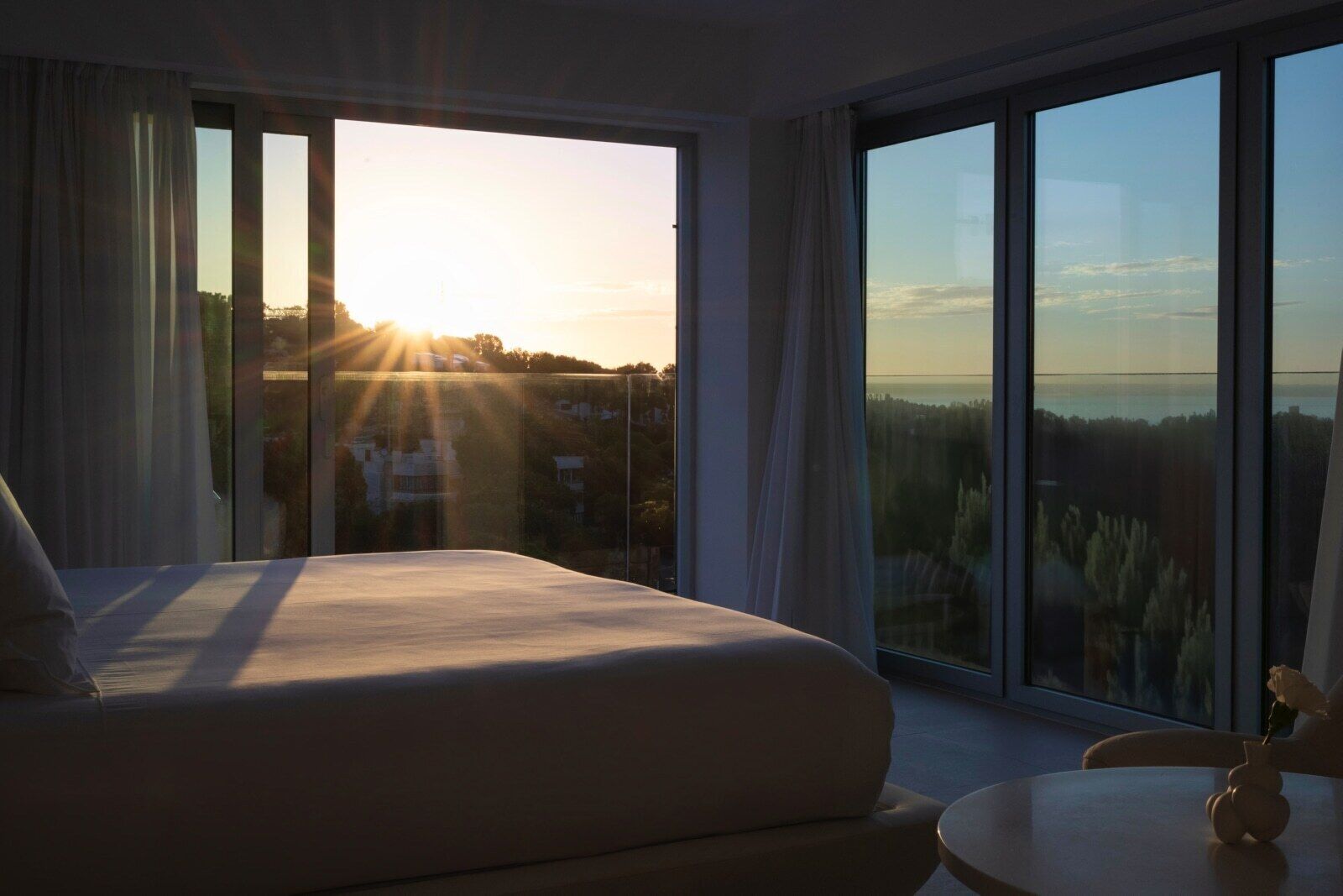 Une chambre dotée d’un grand lit, d’une petite table ronde et offrant une vue sur le paysage urbain grâce à de grandes fenêtres.