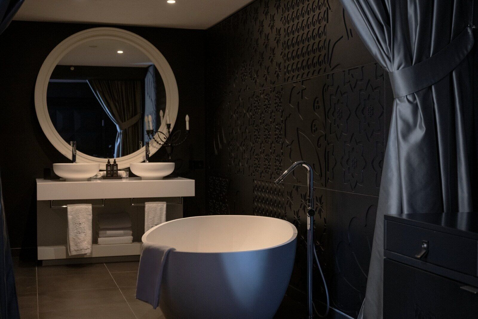 A modern bathroom with a freestanding bathtub, a round mirror, and a vanity with two sinks.