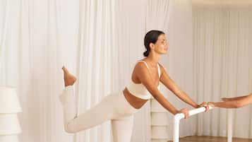A person performing a yoga pose on a mat in a room with white curtains and a wooden floor.