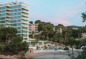 A modern hotel with multiple floors, surrounded by lush greenery and a hillside.
