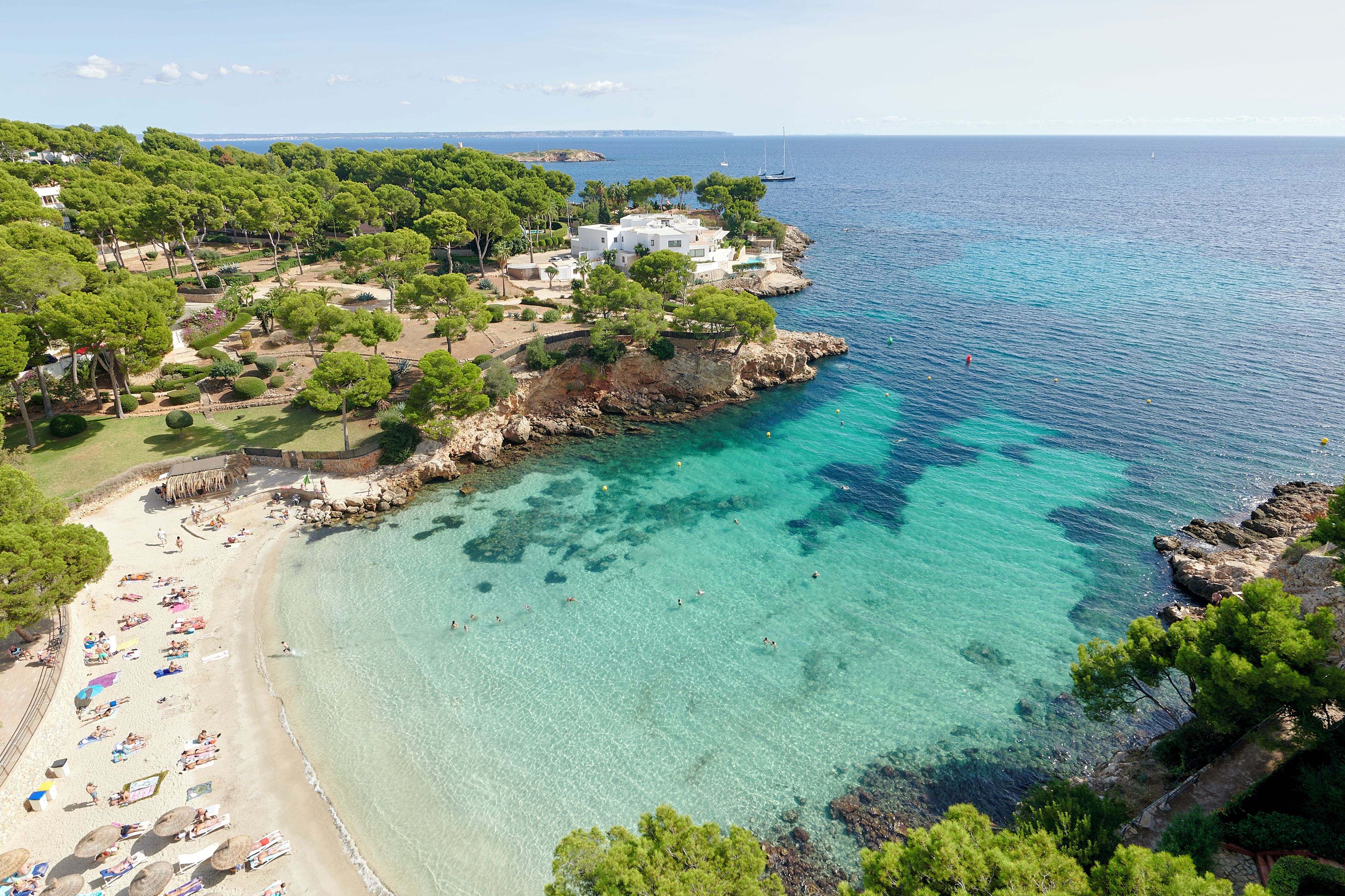 A coastal area with a beach, clear turquoise waters, and a rocky shoreline.