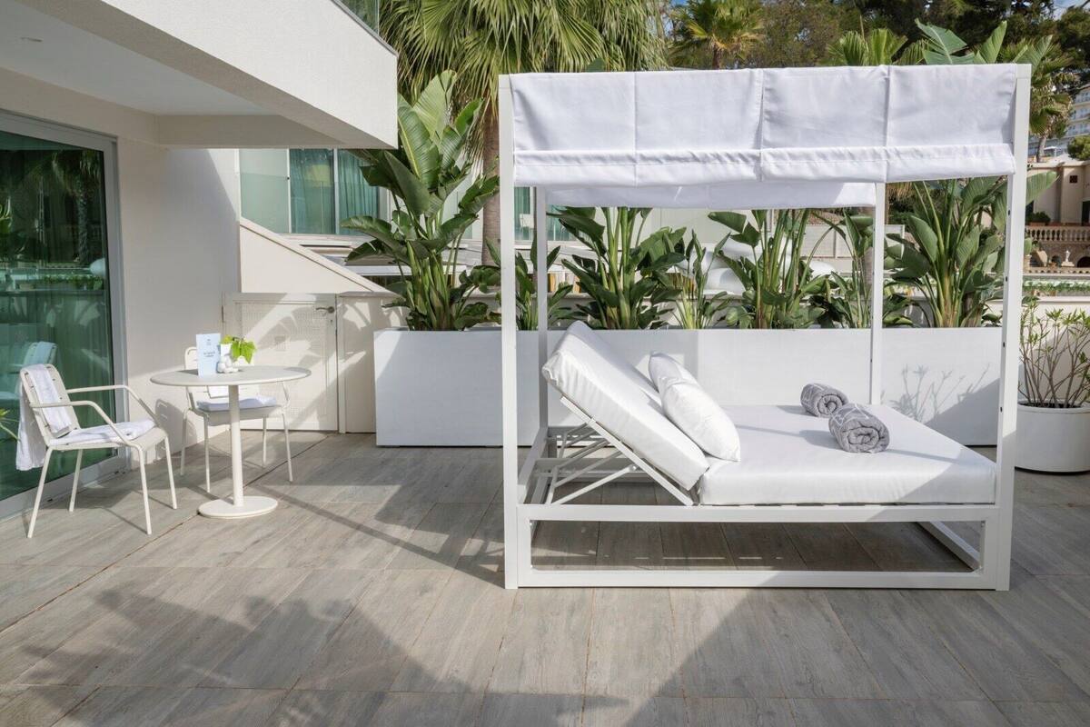 A modern outdoor seating area with a white metal canopy bed, a round table with chairs, and potted plants.