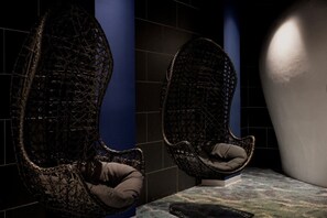 Two wicker chairs with cushions in a dimly lit room with tiled walls and a patterned floor.