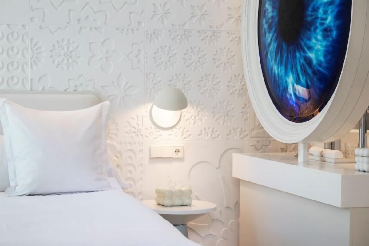 A modern bedroom with a bed, a round mirror, and a small round table.