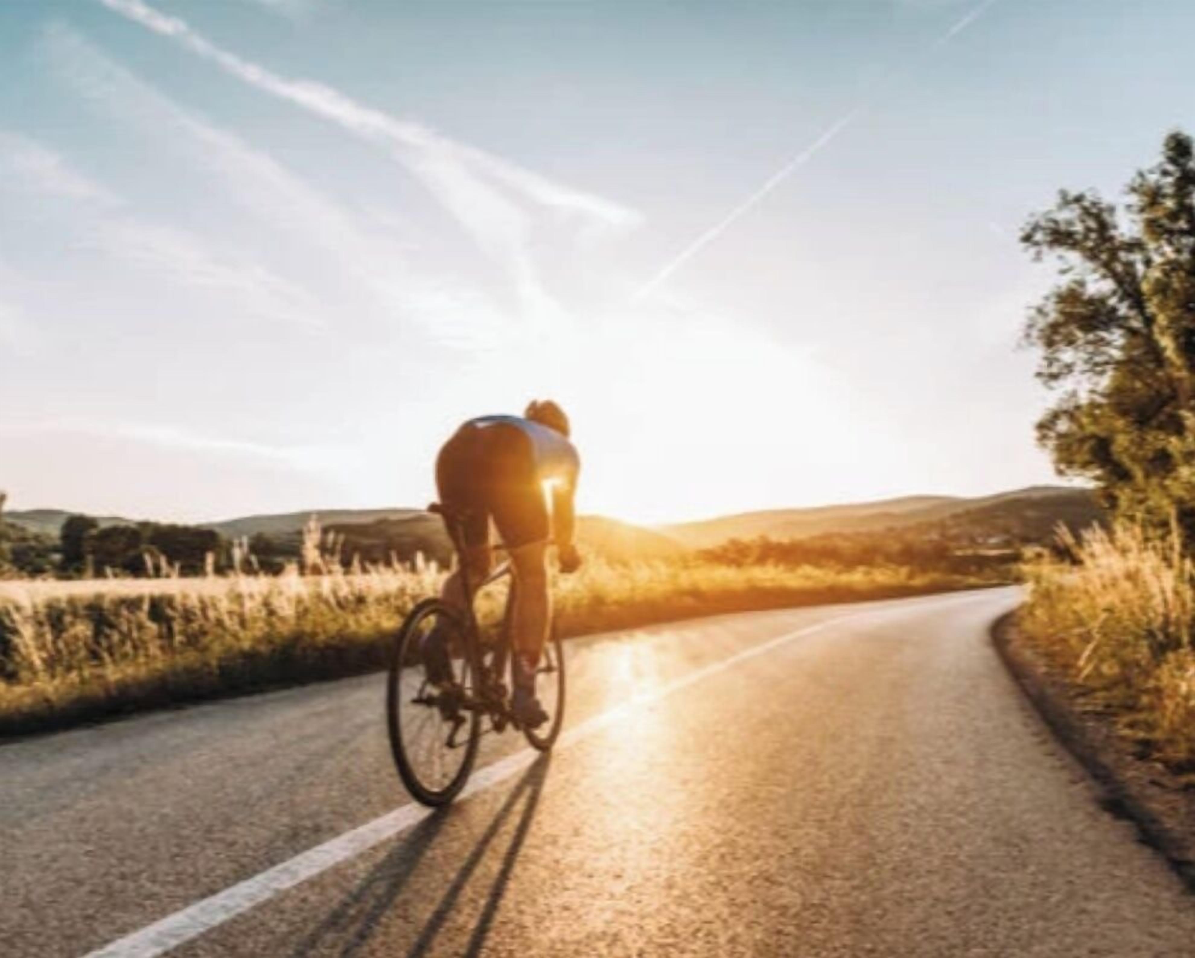 Un ciclista pedaleando por una carretera con cielo despejado y colinas a lo lejos.