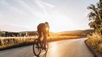 Un ciclista pedaleando por una carretera con cielo despejado y colinas a lo lejos.