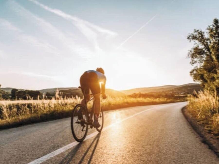 Un ciclista pedaleando por una carretera con cielo despejado y colinas a lo lejos.