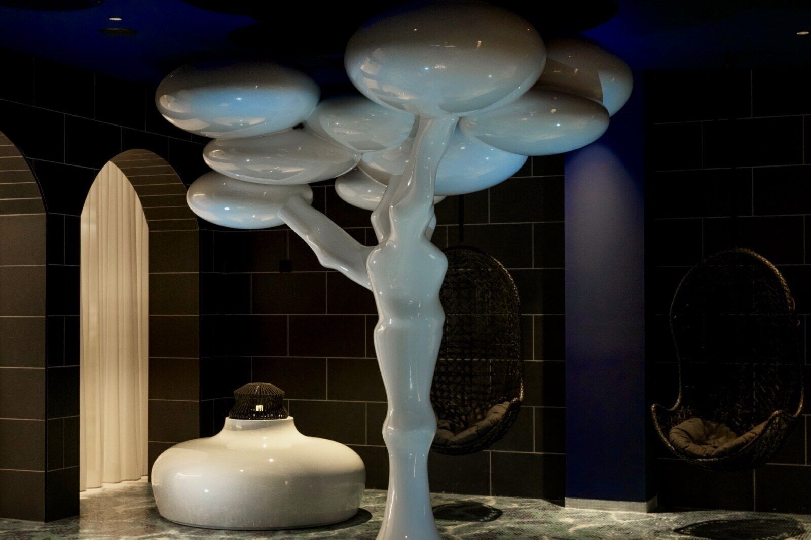 Un interior moderno con una escultura de árbol blanco original, una pared con textura y un sillón colgante.