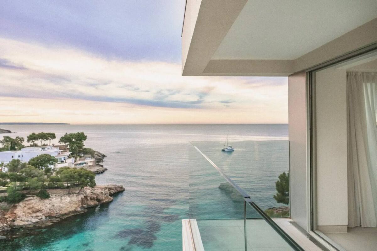 A balcony with a view of the sea, a sailboat, and a distant shoreline with buildings.