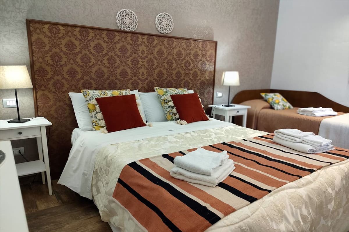 A hotel room with a large bed, two bedside tables, a nightstand, and a small table with a lamp.