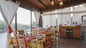 Uma sala de jantar com várias mesas e cadeiras, um armário de madeira com louças e vista para o exterior.