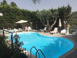 A swimming pool with lounge chairs and umbrellas, surrounded by trees and greenery. - Villa del Sole Relais (Agrigento)