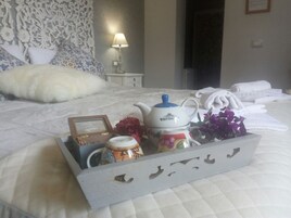 Una cama bien hecha con un cabecero decorativo, una mesita de noche con una lámpara y una bandeja con un hervidor, una taza y una foto enmarcada.
