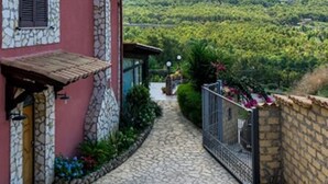 Uma trilha de pedra leva a um edifício com fachada de pedra e vista para uma encosta verde.