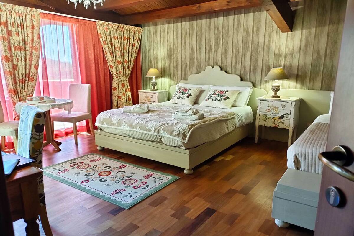 A bedroom with a large bed, two bedside tables with lamps, a chair, a desk, and a patterned rug.