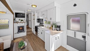 Una cocina moderna para vehículos recreativos, con armarios blancos, estufa de leña, lavamanos y ventana.