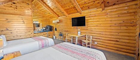 Habitació d'una cabana de fusta amb dos llits, un escriptori, una cadira, una televisió i una xemeneia.