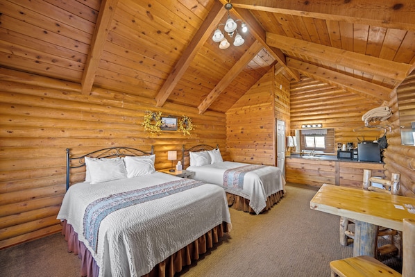 A log cabin room with two beds, a wooden dining table, and a kitchen area.