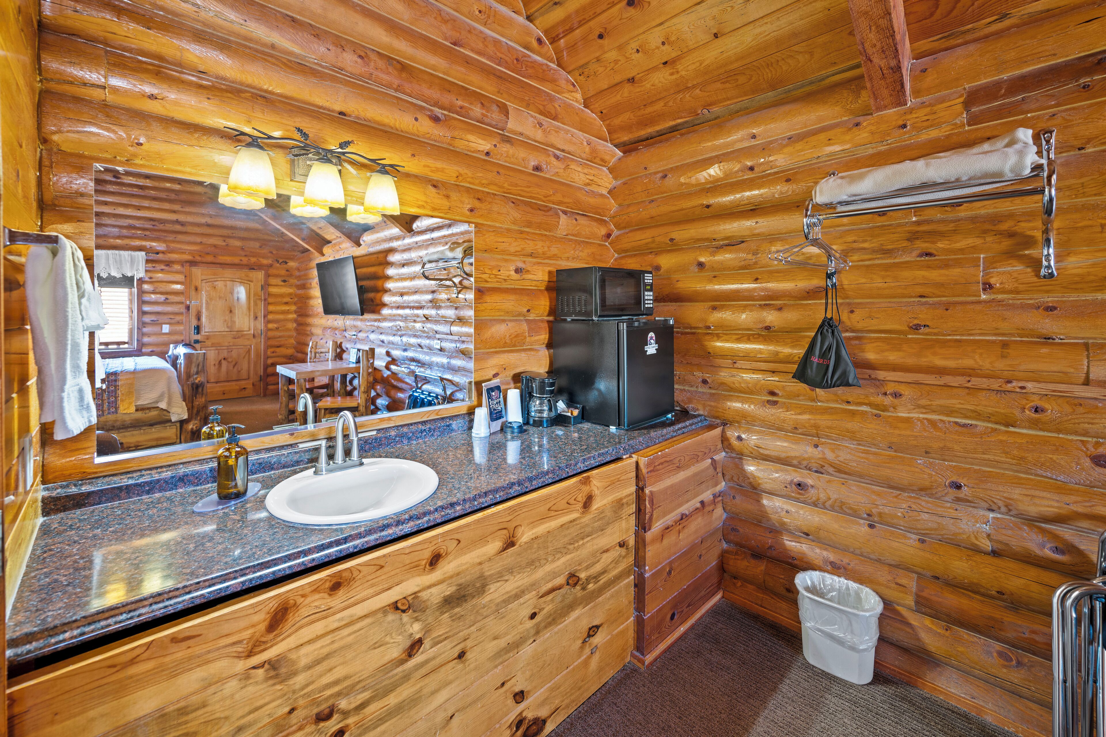 A wooden cabin bathroom with a sink, mirror, and a small refrigerator.
