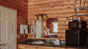 Interior de una cabaña de madera con un baño que incluye un lavamanos, espejo y un refrigerador negro.