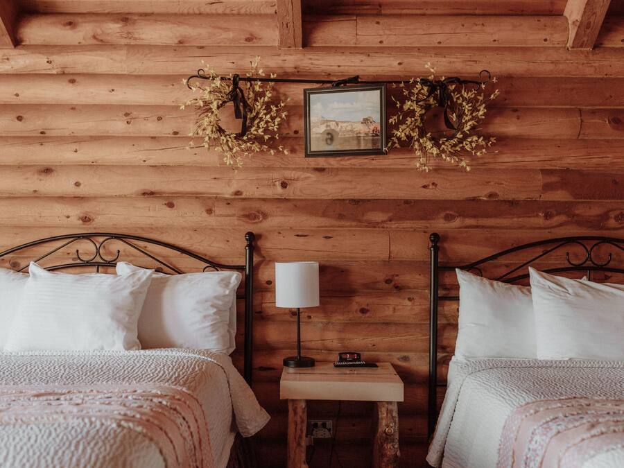 A wooden cabin room with two beds, a nightstand with a lamp, and a framed picture on the wall.
