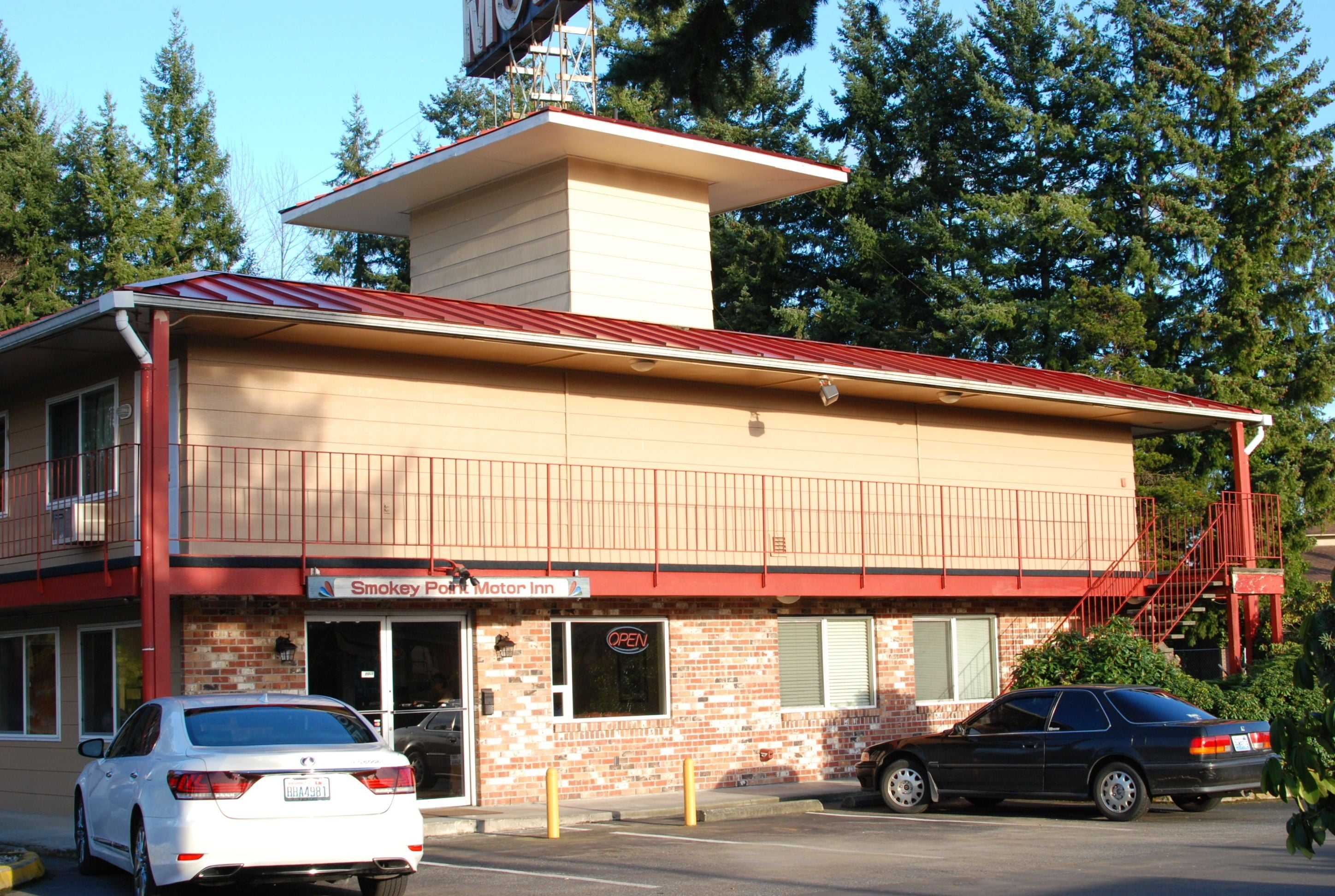 Un edificio de dos pisos con techo rojo y un cartel que dice "Smokey Point Motor Inn". Hay dos coches estacionados adelante.